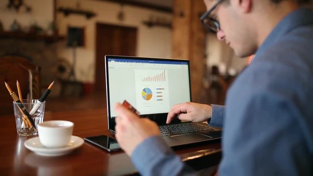 Young man shopping on the internet and paying with credit card. Handsome freelancer businessman in glasses replenish his stock exchange account with laptop via web application. Business concept.