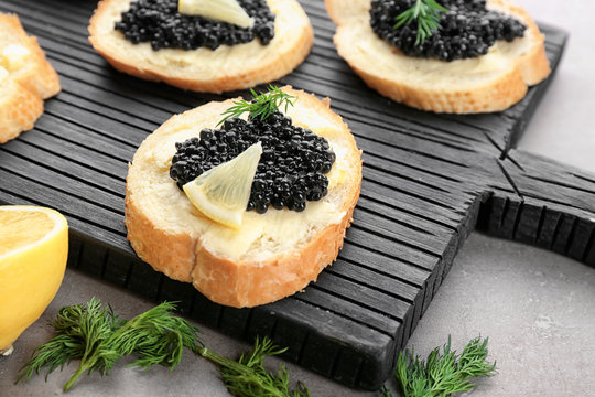 Slices of bread with black caviar and butter on wooden board