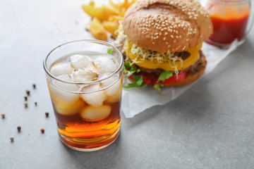 Glass of cold cola with tasty burger on table