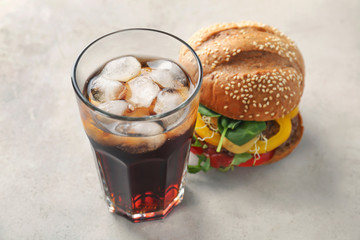 Glass of cold cola with tasty burger on table