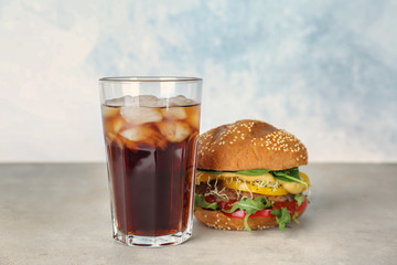 Glass of cold cola with tasty burger on table