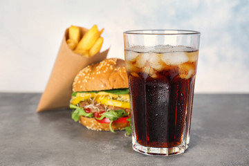 Glass of cold cola with tasty burger on table