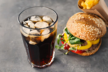 Glass of cold cola with tasty burger on table