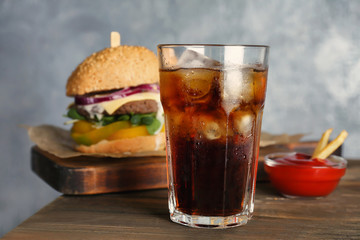 Glass of cold cola with tasty burger on table