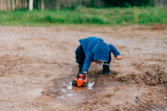 the boy in blue suit plays with a toy car in the dirt