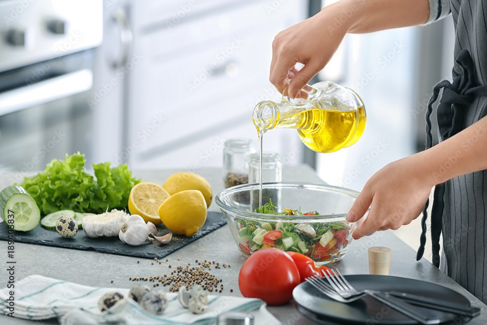 Wall mural woman pouring oil into bowl with fresh vegetable salad on table