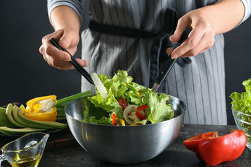 Obraz na płótnie Canvas Woman preparing tasty vegetable salad in bowl on table