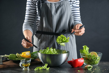 Woman preparing tasty vegetable salad in bowl on table