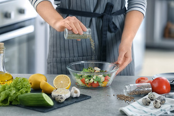 Woman preparing tasty vegetable salad in bowl on table