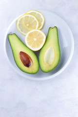Avocado and slices of lemon in a white plate on a white background, green and yellow fruits, tropical fruits, sliced avocado and lemon on a marble background, healthy food, vegan, minimalism