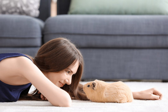 Beautiful young woman with pet guinea pig at home