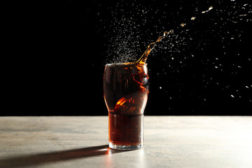 Splash of cola in glass on table against black background