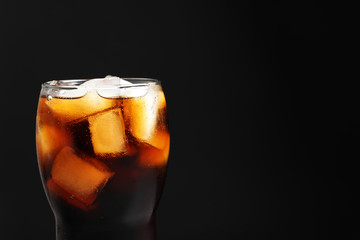 Glass of refreshing cola with ice on black background, closeup