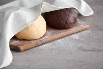Balls of different raw dough covered with towel on table