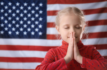 Cute little girl praying on American flag background