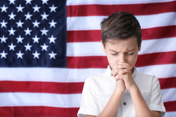 Cute little boy praying on American flag background