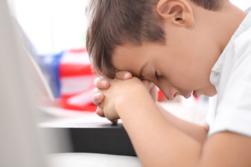 Little boy praying for America over closed Bible indoors