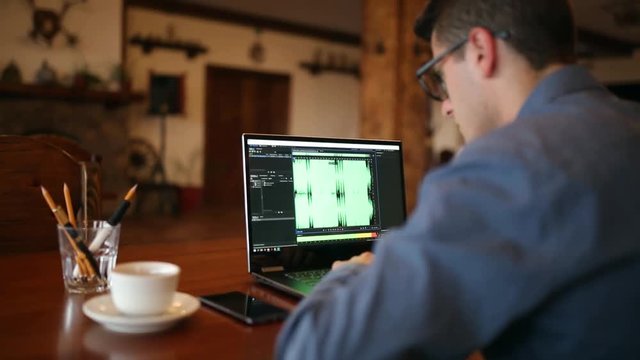 Sound designer or engineer working on laptop with audio mastering software with waveform on screen. Dj man listening to music. Tracking and revealing shot.