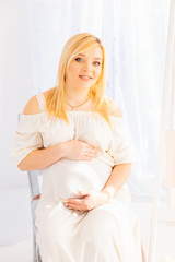 gentle smile of a pregnant woman sitting on a chair on a backgro