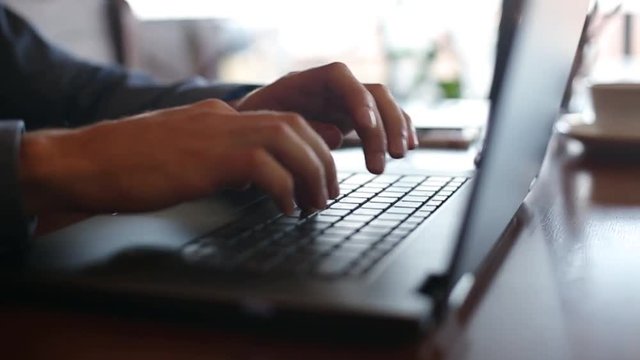 Camera slides around freelancer's hands typing on laptop keyboard in slow motion. Businessman working at office with internet. Cup of coffe on background. Business concept.