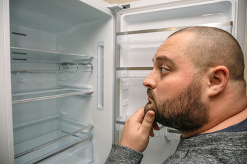 Funny fat man looking into empty fridge
