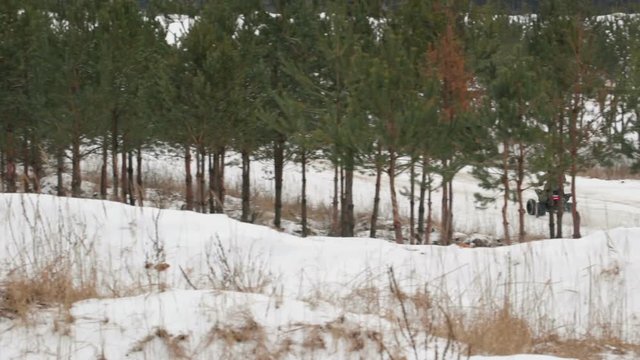 A young guy in a black hat and camouflage jacket passes the turn with a drift on a Quad bike. From the wheels flying dirt and snow.