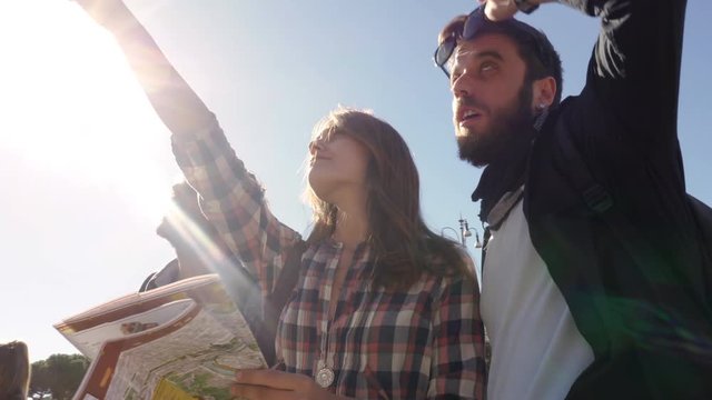 Three young friends tourists standing in front of colosseum in rome reading map guide for directions pointing with backpacks sunglasses happy beautiful girl long hair steadycam camera spinning around