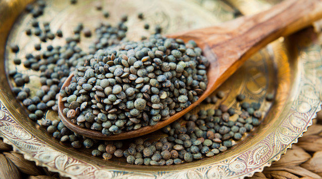 Puy Lentils -  French Green legume, dried grains on wooden spoon.