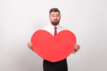 Bearded man thoughtful, holding red heart and thinking of love