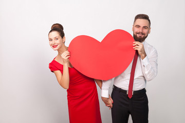 Attractive couple toothy smile, look out from behind big heart