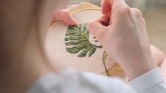 The woman is embroidering a picture of a flower leaf on the fabric. Home Crafts