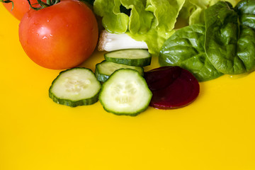 Fresh colourful salad ingredients, yellow background, room for text. Lettuce, spring onion, tomato, beetroot and cucumber slices, closeup.