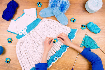 Dressmaker workplace. Female woman knitting on wooden background making blue dress for baby girls