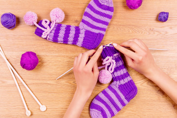 Woman female girl knits a new warm striped violet socks on wooden background. Dressmaker workplace. Top view