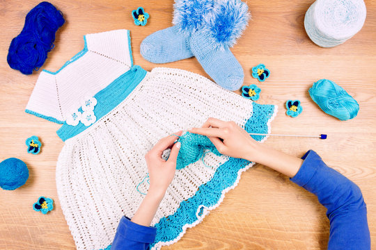 Dressmaker workplace. Female woman knitting on wooden background making blue dress for baby girls