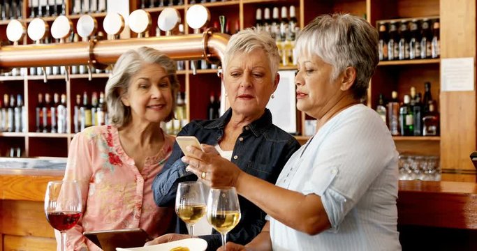 Senior friends using mobile phone while having wine