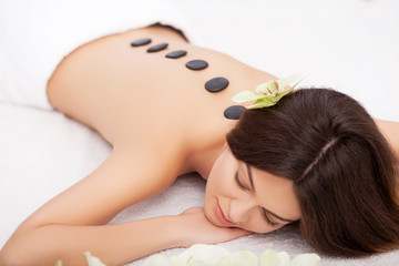 Obraz na płótnie Canvas Spa. Young woman doing hot stone therapy. Professional beautician massaging female back by stones