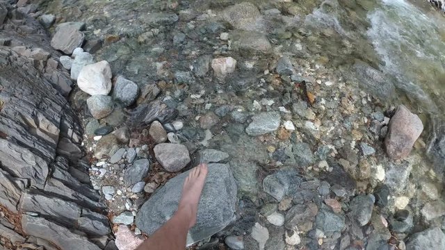 Traveler explores a mountain river. It moves up the river. He has in his hands an action camera with a stabilizer.