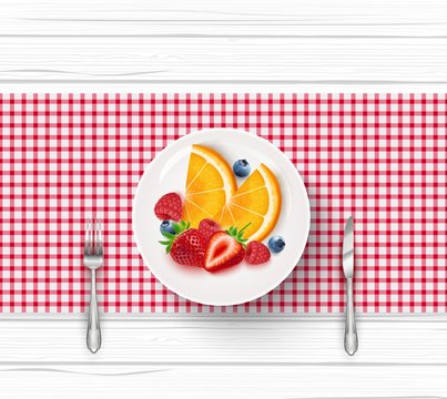 Fresh fruit salad in white saucer with fork and knife on wooden table