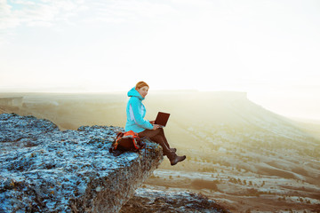 woman working with laptop sitting on the rocky mountain 

