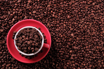 Red coffee cup and saucer one single for espresso or capuccino filled full of coffee bean on a background of scattered dark coffee beans photo top view