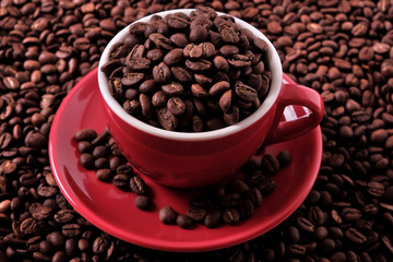 Red coffee cup and saucer one single for espresso or capuccino filled full of coffee bean on a background of scattered dark coffee beans photo