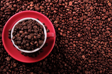 Red coffee cup and saucer one single for espresso or capuccino filled full of coffee bean on a background of scattered dark coffee beans photo top view