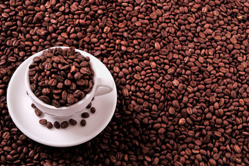 White coffee cup and saucer one single for espresso or capuccino filled full of coffee bean on a background of scattered dark coffee beans photo