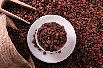 White coffee cup and saucer one single for espresso or capuccino filled full of coffee bean on a background of scattered dark coffee beans photo