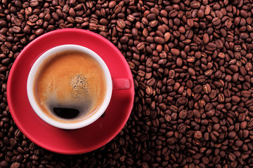 Red coffee cup and saucer one single for espresso or capuccino on a background of scattered dark coffee beans photo top view