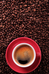 Red coffee cup and saucer one single for espresso or capuccino on a background of scattered dark coffee beans photo vertical