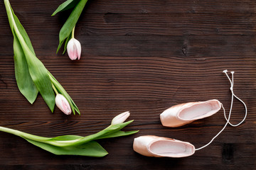 Ballet pointe shoes near spring tulips on dark wooden background top view copy space