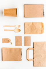 Obraz na płótnie Canvas Disposable tableware. Paper cup, spoon, fork near brown paper bag, label and notebook top view mock up pattern white background