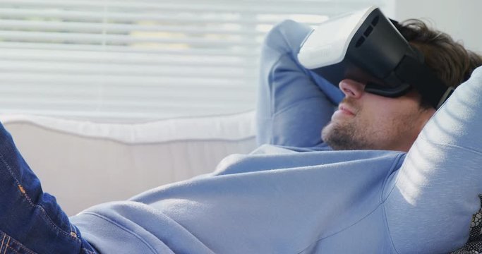 Young man lying on sofa wearing virtual reality headset at  home  